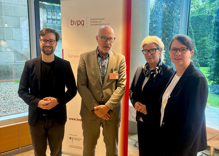 Vier Personen stehen beim Parlamentarischen Fr&uuml;hst&uuml;ck 2026 vor einem Roll-up der Bundesvereinigung Pr&auml;vention und Gesundheitsf&ouml;rderung e.V. und posieren f&uuml;r ein gemeinsames Foto.