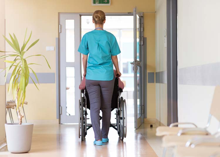 Pflegerin schiebt Rollstuhl durch Flur