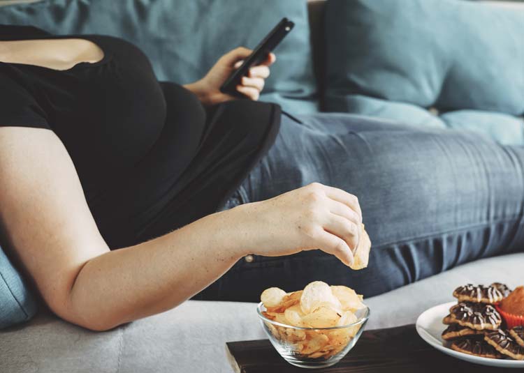Übergewichtige Frau liegt mit Chips auf Sofa
