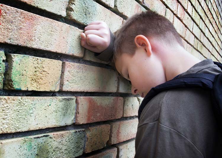 Trauriger Junge lehnt Kopf an Hausmauer