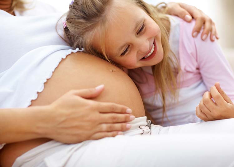 Kleines M&auml;dchen lauscht an Schwangerenbauch