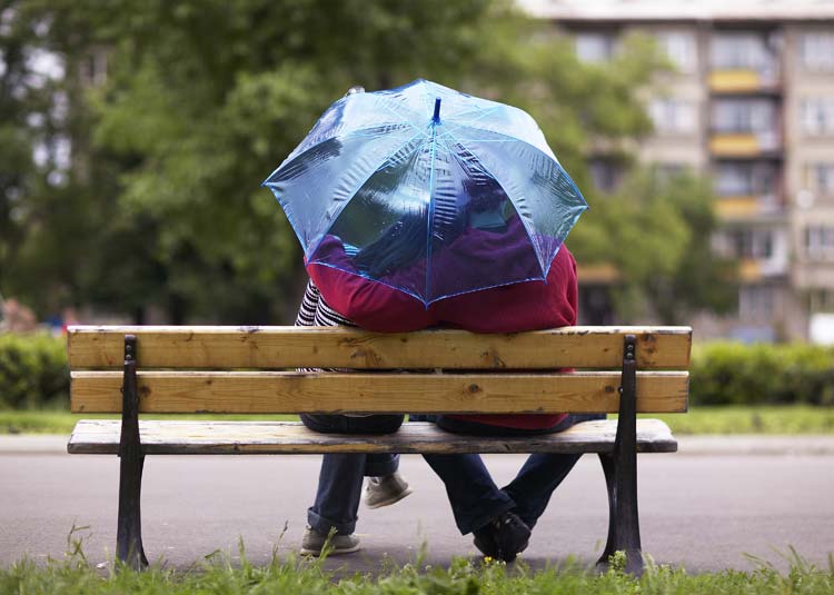 Paar sitzt auf Bank mit Regenschirm
