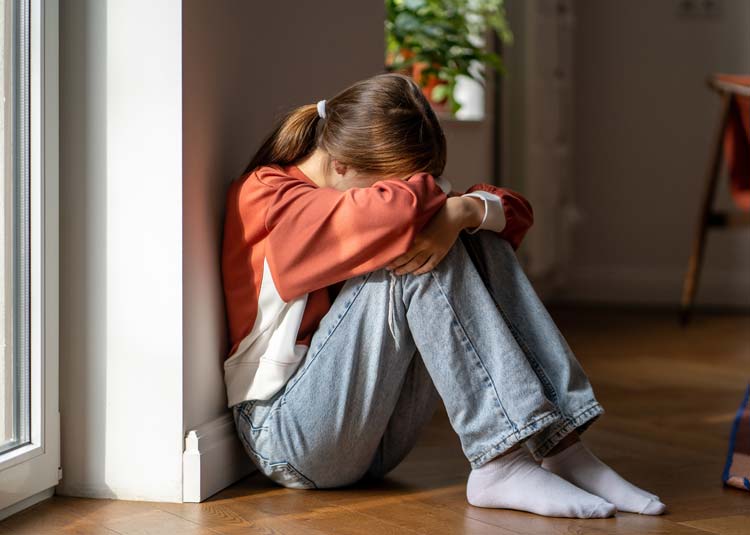 Unglückliches jugendliches Mädchen sitzt am Boden, weint und hält sich die Hände vor das Gesicht