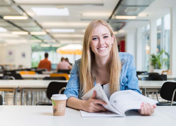 Studentin mit Buch und Kaffee in Mensa